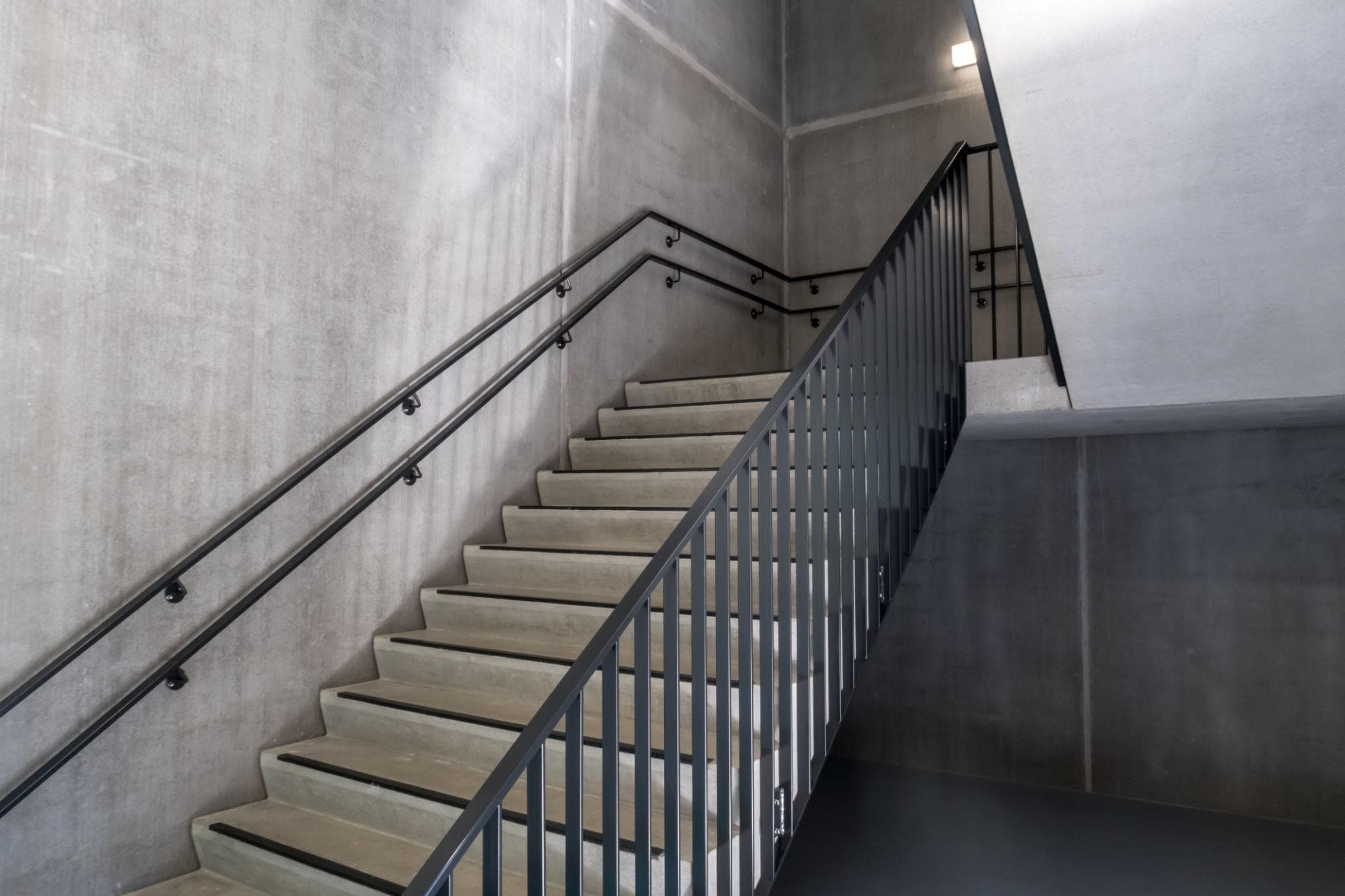 Leeres Treppenhaus aus Sichtbeton mit Stahlgeländer.